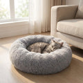 Tabby cat asleep in a grey CloudNest calming donut bed beside a linen sofa